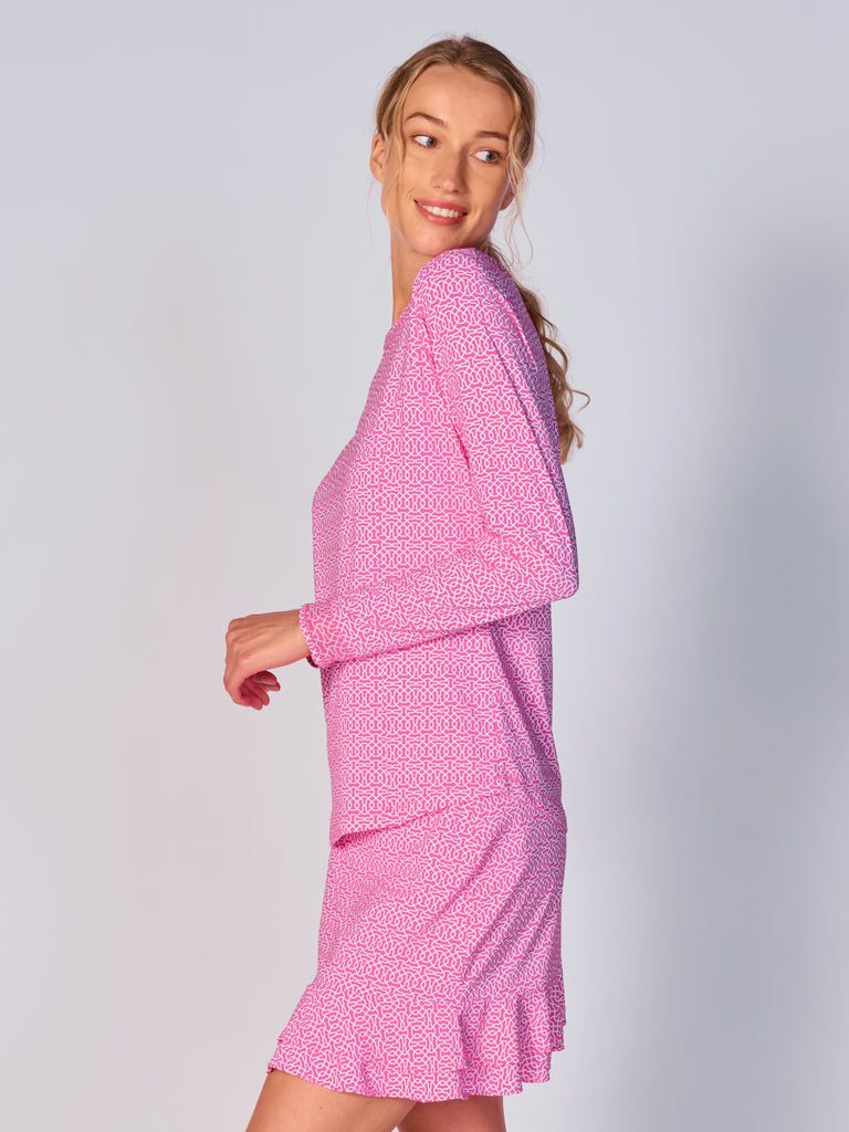 A woman is showcasing the side of the G Lifestyle Mesh Block Long Sleeve Top in Cubic Hot Pink - geometric print of the Spring Summer 2024 Collection. The top is designed with long sleeves, mesh underarm inserts for breathability, and features a round neckline with texture mesh block detailing around it and sleeve hems. The fabric appears to be lightweight, movement-friendly, with subtle texture. Suitable for various outdoor athletic activities such as golf, tennis, padel tennis, pickleball or even cycling.
