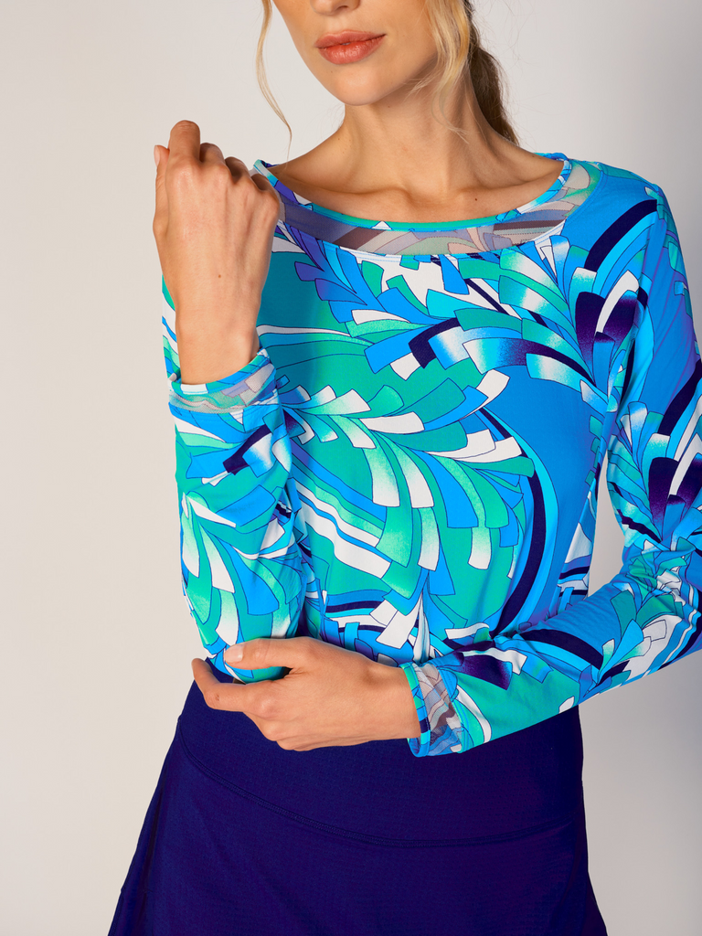 A woman wears G Lifestyle Mesh Block Long Sleeve Top in St Barths Blue - abstract print of the Spring Summer 2024 Collection. The top is designed with long sleeves, mesh underarm inserts for breathability, and features a round neckline with texture mesh block detailing around it and sleeve hems. The fabric appears to be lightweight, movement-friendly, with subtle texture. Suitable for various outdoor athletic activities such as golf, tennis, padel tennis, pickleball or even cycling.