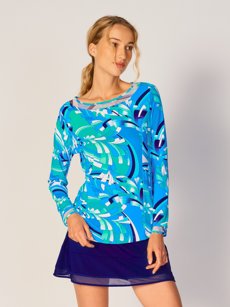 A woman wears G Lifestyle Mesh Block Long Sleeve Top in St Barths Blue - abstract print of the Spring Summer 2024 Collection. The top is designed with long sleeves, mesh underarm inserts for breathability, and features a round neckline with texture mesh block detailing around it and sleeve hems. The fabric appears to be lightweight, movement-friendly, with subtle texture. Suitable for various outdoor athletic activities such as golf, tennis, padel tennis, pickleball or even cycling.