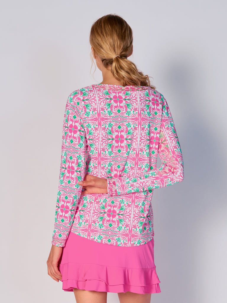 A woman is showcasing the back of the G Lifestyle Mesh Block Long Sleeve Top in Pink Tile – symmetrical ornamental print of the Spring Summer 2024 Collection. The top is tailored with a snug fit silhouette, complete with long sleeves and round neckline with mesh details. Notably, it includes smooth mesh underarm inserts, which are seamlessly integrated for enhanced breathability, ensuring comfort during active use. 
