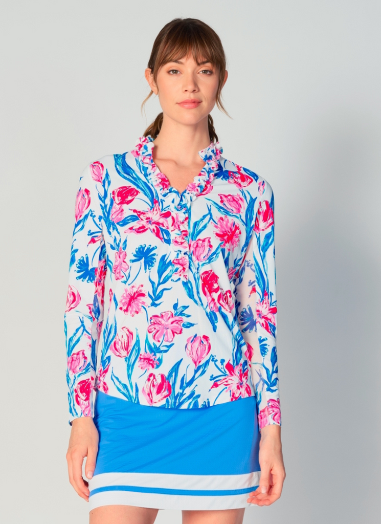 A woman wears G Lifestyle UPF 50+ Ruffle V Neck Top in Tulip - floral print of the Spring Summer 2024 Collection. The top is designed with long sleeves, mesh underarm inserts for breathability, and features a delicately ruffled V-neckline adding feminine touch to the sporty style. The fabric appears to be lightweight, movement-friendly, with subtle texture. Suitable for various outdoor athletic activities such as golf, tennis, padel tennis, pickleball or even cycling.