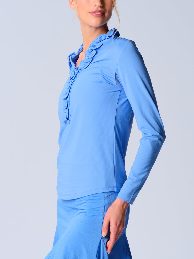 A woman is showcasing the side of the G Lifestyle UPF 50+ Ruffle V Neck Top in Bright Peri. The top is tailored with a snug fit silhouette, complete with long sleeves and a v-neckline with ruffle details. Notably, it includes smooth mesh underarm inserts, which are seamlessly integrated for enhanced breathability, ensuring comfort during active use. 