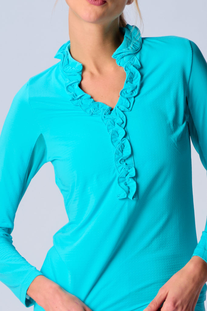 A woman wears G Lifestyle UPF 50+ Ruffle V Neck Top in Caribbean Turquoise. The top is designed with long sleeves, mesh underarm inserts for breathability, and features a delicately ruffled V-neckline adding feminine touch to the sporty style. The fabric appears to be lightweight, movement-friendly, with subtle texture. Suitable for various outdoor athletic activities such as golf, tennis, padel tennis, pickleball or even cycling.