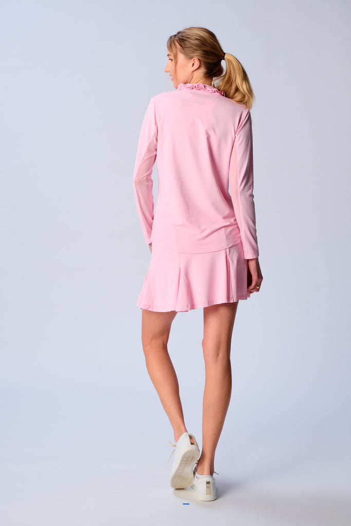 A woman is showcasing the back of the G Lifestyle UPF 50+ Ruffle V Neck Top in Light Pink. The top is tailored with a snug fit silhouette, complete with long sleeves and a v-neckline with ruffle details. Notably, it includes smooth mesh underarm inserts, which are seamlessly integrated for enhanced breathability, ensuring comfort during active use. 