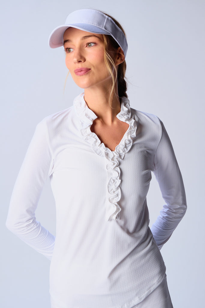 A woman wears G Lifestyle UPF 50+ Ruffle V Neck Top in White. The top is designed with long sleeves, mesh underarm inserts for breathability, and features a delicately ruffled V-neckline adding feminine touch to the sporty style. The fabric appears to be lightweight, movement-friendly, with subtle texture. Suitable for various outdoor athletic activities such as golf, tennis, padel tennis, pickleball or even cycling.