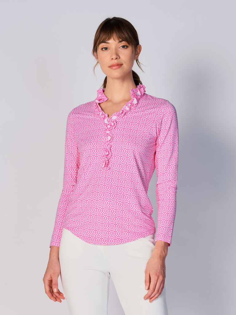 A woman wears G Lifestyle UPF 50+ Ruffle V Neck Top in Cubic Hot Pink - geometric print of the Spring Summer 2024 Collection. The top is designed with long sleeves, mesh underarm inserts for breathability, and features a delicately ruffled V-neckline adding feminine touch to the sporty style. The fabric appears to be lightweight, movement-friendly, with subtle texture. Suitable for various outdoor athletic activities such as golf, tennis, padel tennis, pickleball or even cycling.
