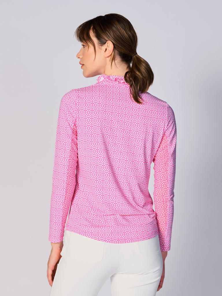 A woman is showcasing the back of the G Lifestyle UPF 50+ Ruffle V Neck Top in Cubic Hot Pink - geometric print of the Spring Summer 2024 Collection. The top is tailored with a snug fit silhouette, complete with long sleeves and a v-neckline with ruffle details. Notably, it includes smooth mesh underarm inserts, which are seamlessly integrated for enhanced breathability, ensuring comfort during active use. 