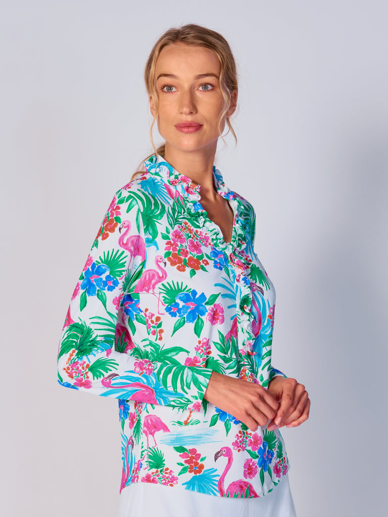 A woman is showcasing the side of the G Lifestyle UPF 50+ Ruffle V Neck Top in Flamingo - tropical print of the Spring Summer 2024 Collection. The top is tailored with a snug fit silhouette, complete with long sleeves and a v-neckline with ruffle details. Notably, it includes smooth mesh underarm inserts, which are seamlessly integrated for enhanced breathability, ensuring comfort during active use. 