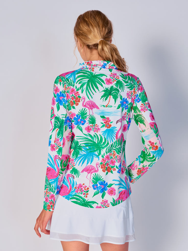 A woman is showcasing the back of the G Lifestyle UPF 50+ Ruffle V Neck Top in Flamingo - tropical print of the Spring Summer 2024 Collection. The top is tailored with a snug fit silhouette, complete with long sleeves and a v-neckline with ruffle details. Notably, it includes smooth mesh underarm inserts, which are seamlessly integrated for enhanced breathability, ensuring comfort during active use. 