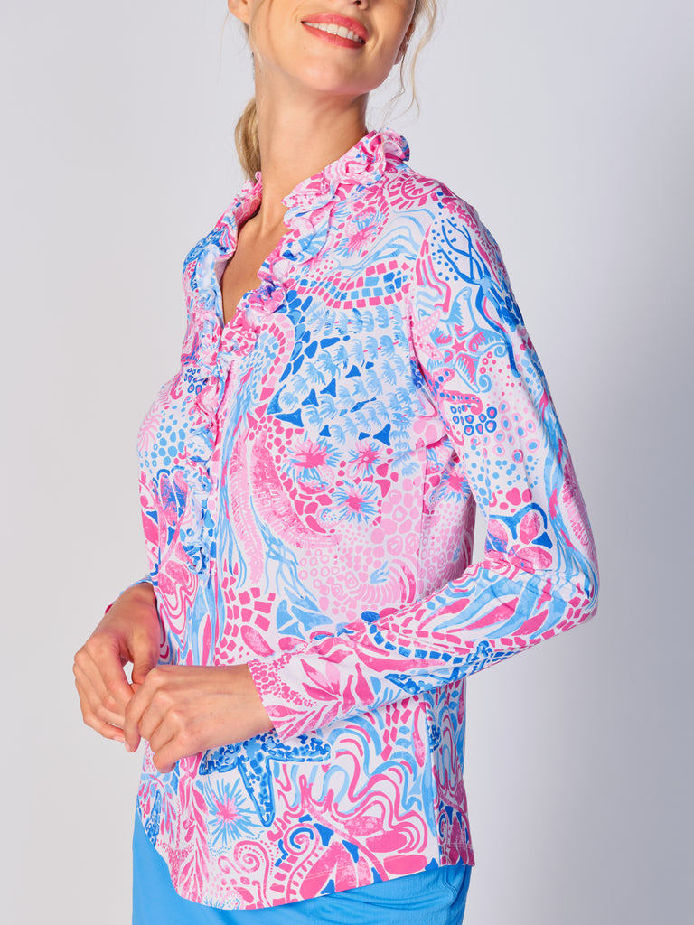 A woman is showcasing the side of the G Lifestyle UPF 50+ Ruffle V Neck Top in Starfish Pink – sea-theme print of the Spring Summer 2024 Collection. The top is tailored with a snug fit silhouette, complete with long sleeves and a v-neckline with ruffle details. Notably, it includes smooth mesh underarm inserts, which are seamlessly integrated for enhanced breathability, ensuring comfort during active use. 