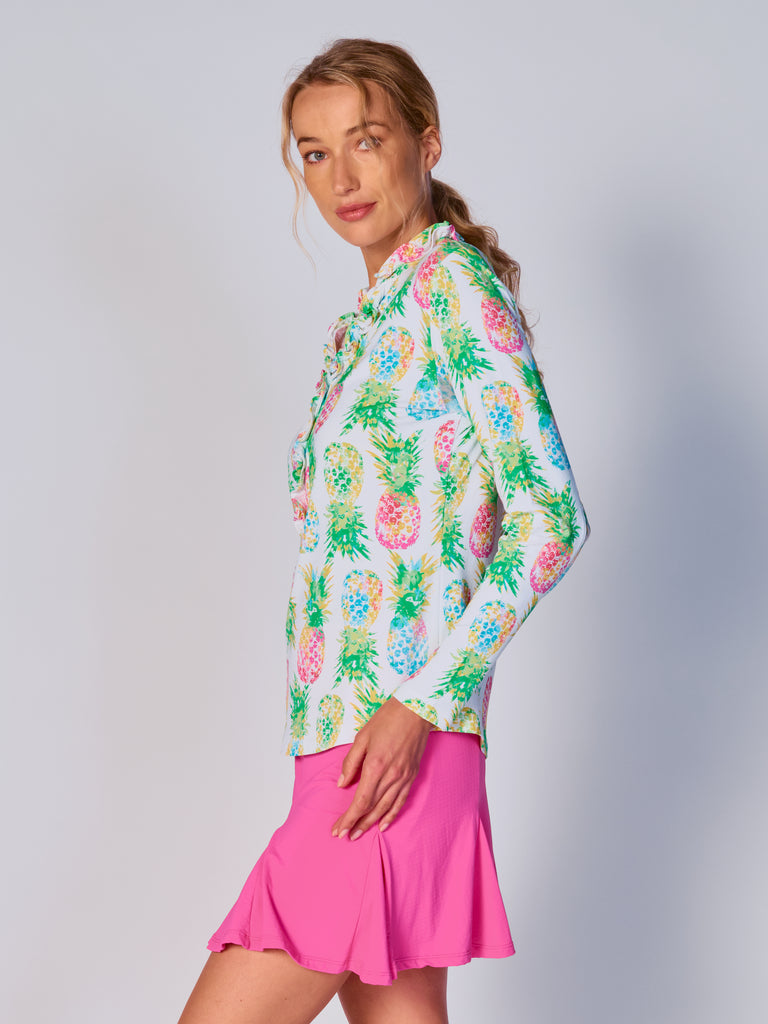 A woman is showcasing the side of the G Lifestyle UPF 50+ Ruffle V Neck Top in Ananas Green - tropical print of the Spring Summer 2024 Collection. The top is tailored with a snug fit silhouette, complete with long sleeves and a v-neckline with ruffle details. Notably, it includes smooth mesh underarm inserts, which are seamlessly integrated for enhanced breathability, ensuring comfort during active use. 