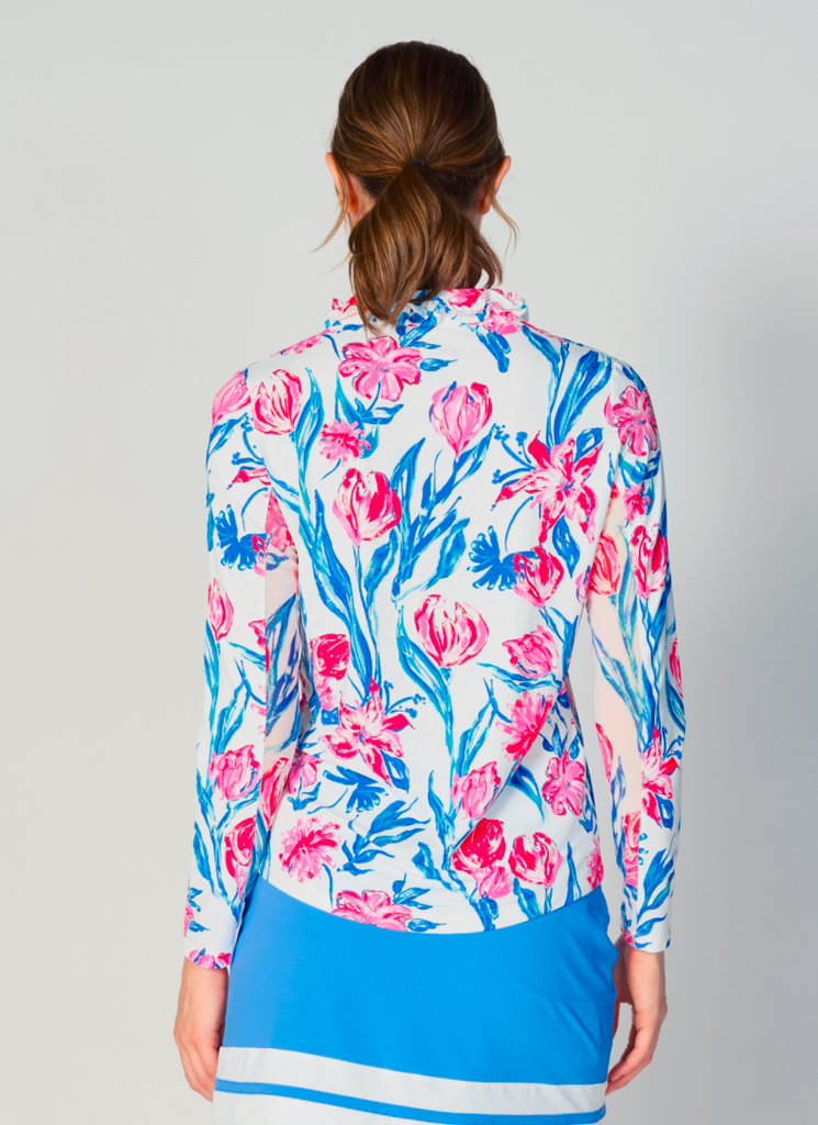 A woman is showcasing the back of the G Lifestyle UPF 50+ Ruffle V Neck Top in Tulip - floral print of the Spring Summer 2024 Collection. The top is tailored with a snug fit silhouette, complete with long sleeves and a v-neckline with ruffle details. Notably, it includes smooth mesh underarm inserts, which are seamlessly integrated for enhanced breathability, ensuring comfort during active use. 