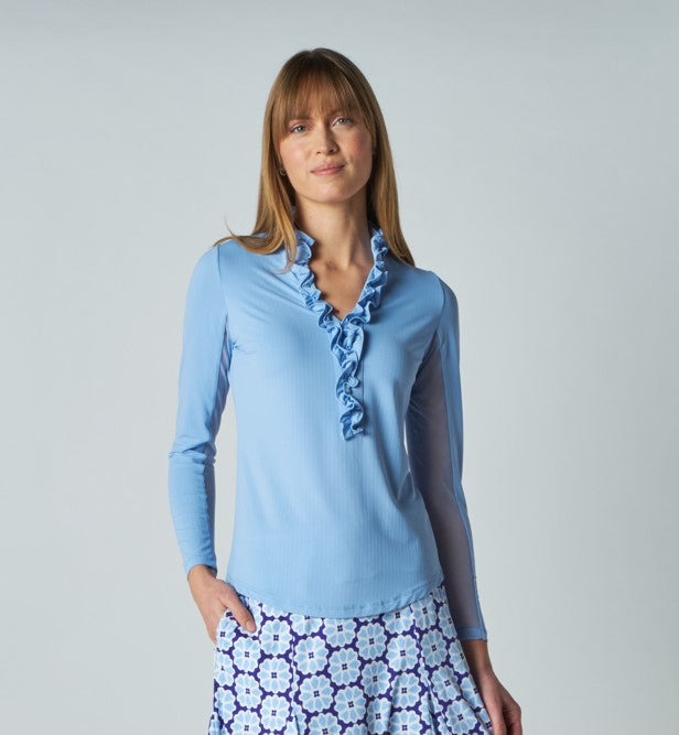 A woman wears G Lifestyle UPF 50+ Ruffle V Neck Top in Light Blue. The top is designed with long sleeves, mesh underarm inserts for breathability, and features a delicately ruffled V-neckline adding feminine touch to the sporty style. The fabric appears to be lightweight, movement-friendly, with subtle texture. Suitable for various outdoor athletic activities such as golf, tennis, padel tennis, pickleball or even cycling.