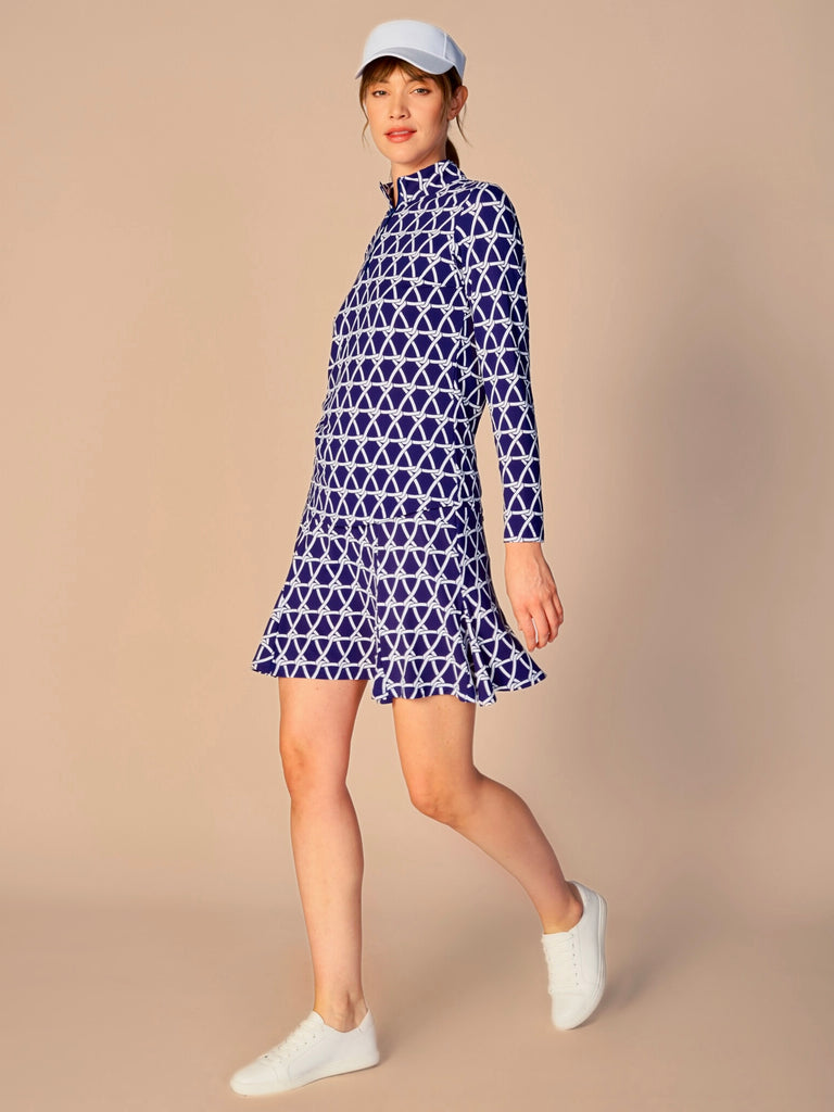A woman pictured while twirling, showcasing the G Lifestyle Flare Godet Skort in Nautical True Navy – marine-inspired rope-knot print from Spring Summer 2024 Collection. This feminine and sporty skort features a fitted waistband and a flared hem with godet inserts, giving the garment playful and flirty silhouette. The length of the skort appears to be mid-thigh. The fabric looks soft, comfortable, and stretchy. This skort is suitable for tennis, pickleball, padel tennis, golf.